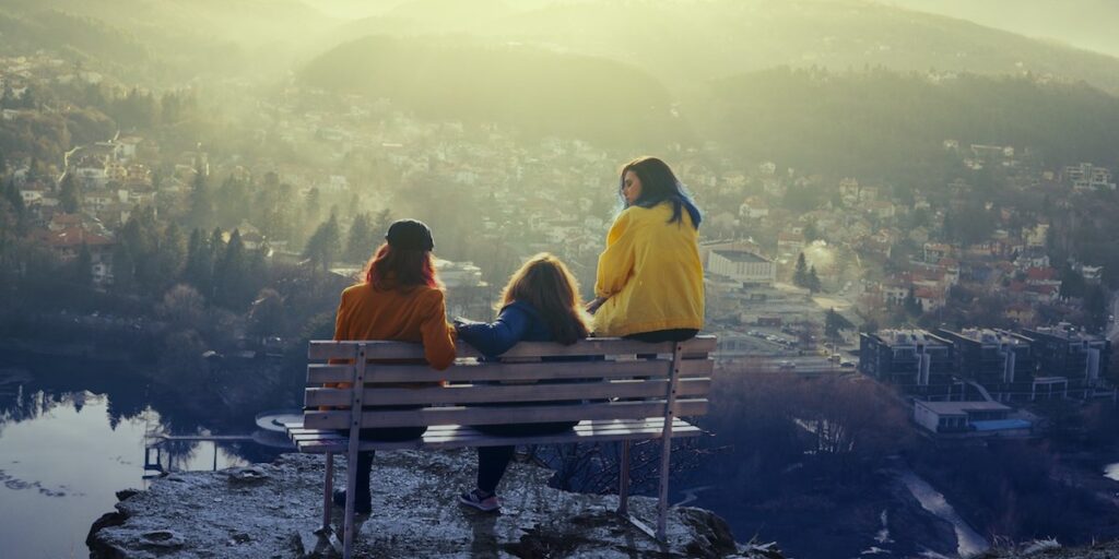 People of Maha - седнали на пейка с гръб към камерата и гледащи града. Снимка от корицата на дебютния им албум "Blue to Gold"